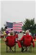 Couple Sitting in Lawn Chairs Facing a Stage with an American Flag